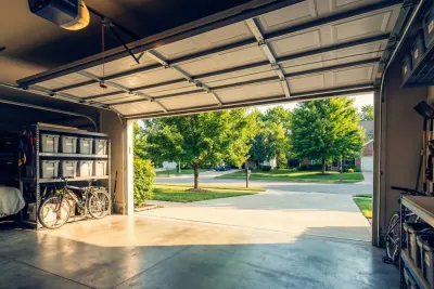 A clean, open garage with bicycles and storage bins inside, looking out onto a sunny suburban street lined with green trees and well-kept lawns.