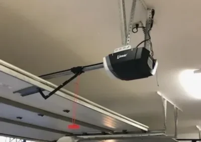 A garage door opener is mounted to the ceiling, but the motor is installed backward, facing away from the door. The metal track and arm are misaligned, preventing proper door operation.