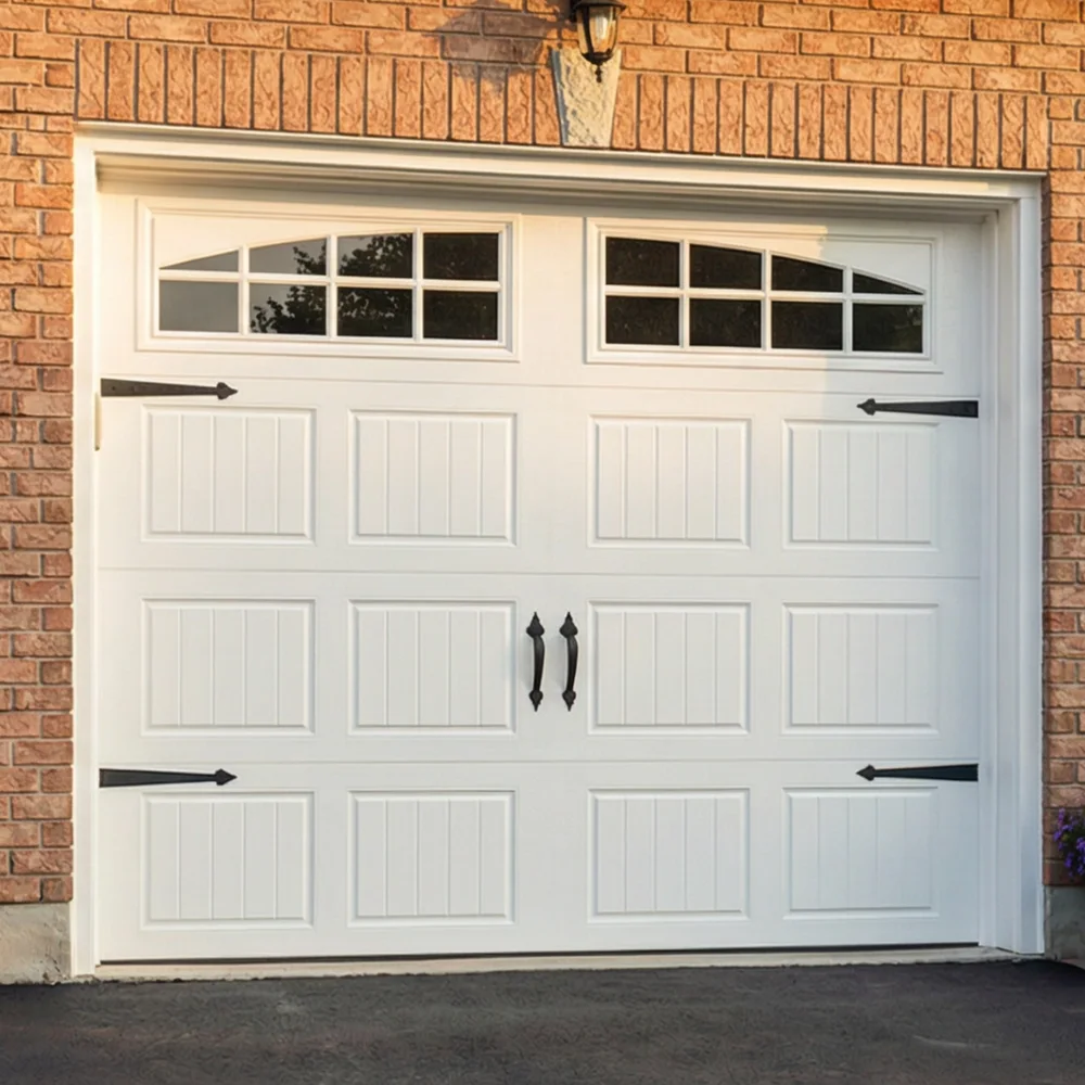 White garage door with decorative black handles and hinges, featuring four upper window panels. The door is set in a brick wall with a lit exterior light above. The driveway is paved with asphalt. White garage door with decorative black handles and hinges, featuring four upper window panels. The door is set in a brick wall with a lit exterior light above. The driveway is paved with asphalt.